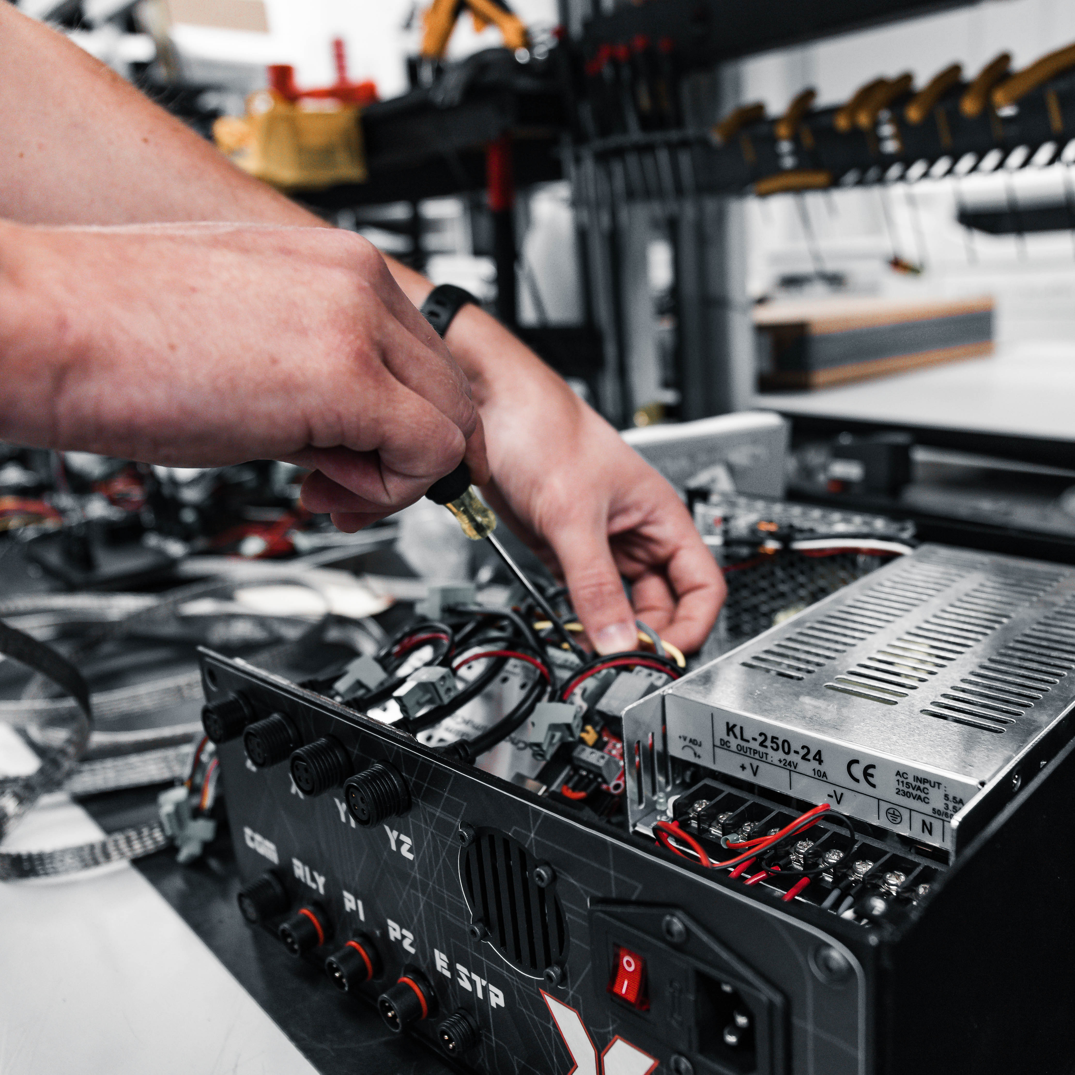 Person working on electronic equipment with a screwdriver in a workshop setting