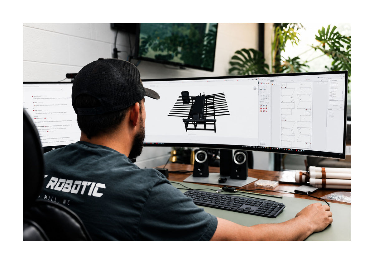 Engineer working at a desk with dual monitors, one displaying a 3D model of a machine.