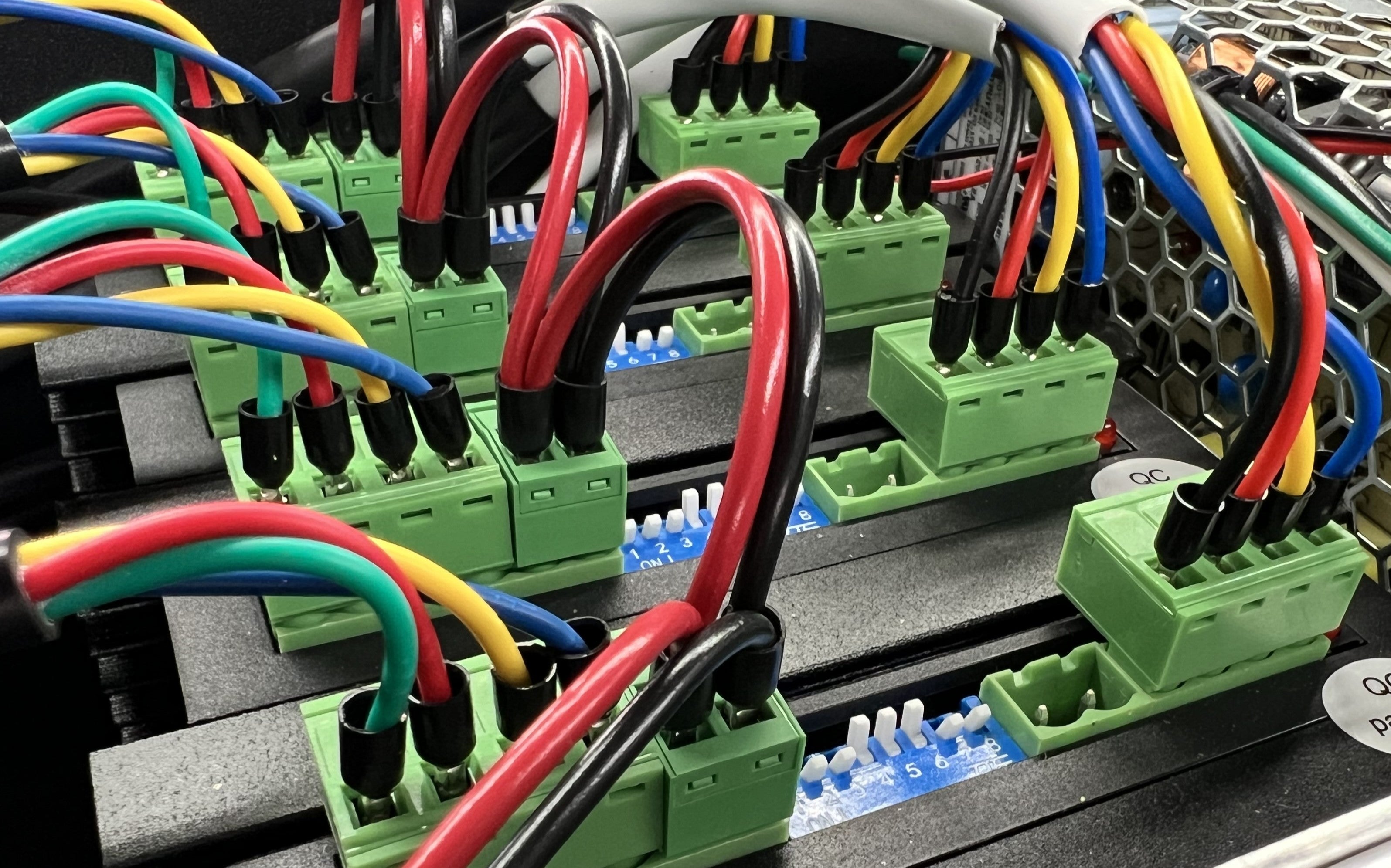 Close-up of colorful wires connected to green terminal blocks on a metallic surface.
