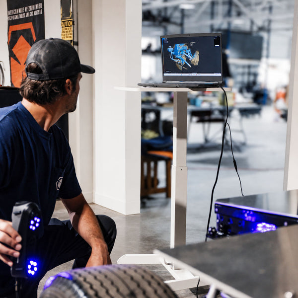 Person using a 3D scanner with a laptop displaying 3D model in a workshop setting
