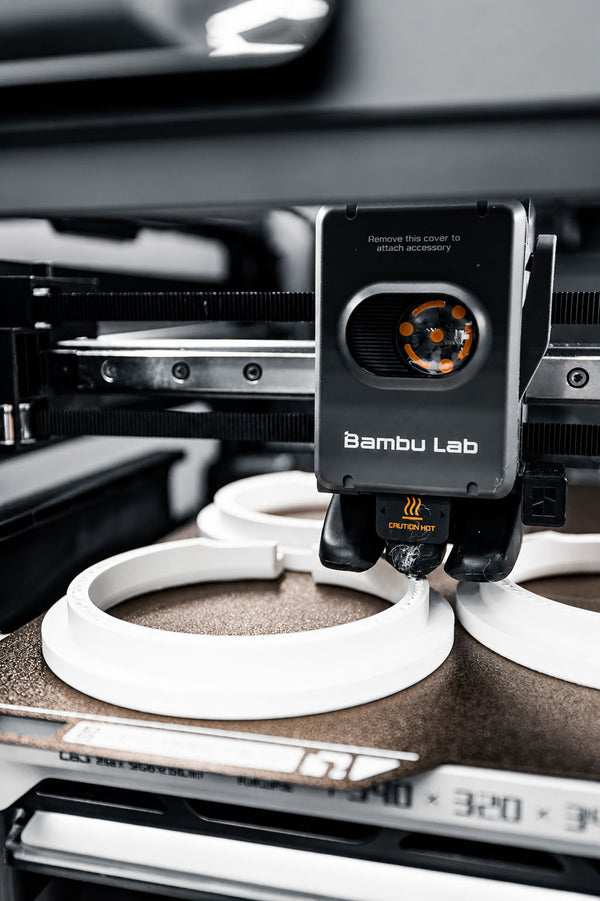 FDM 3D printer in action with a white print on the bed, branded 'Bambu Lab'.