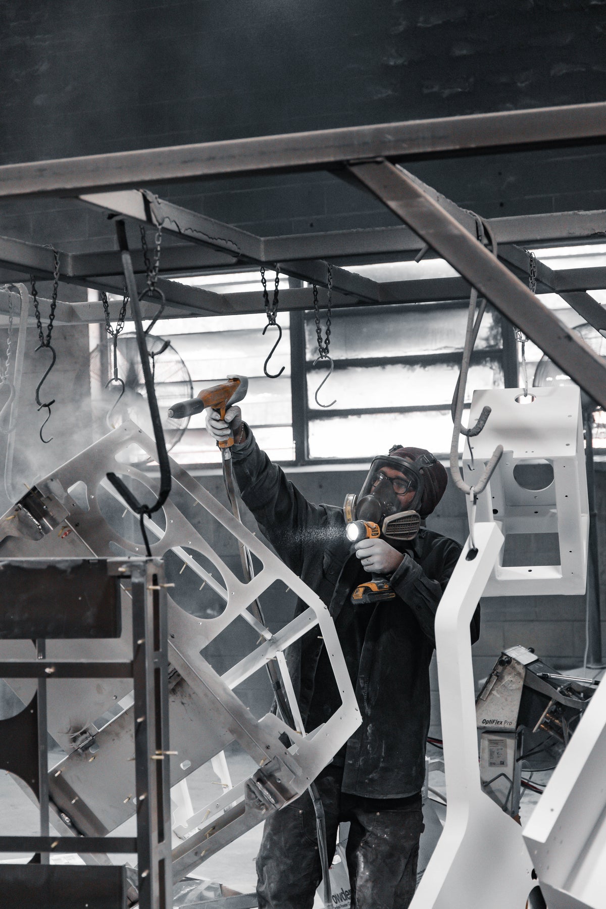 Person powder coating a large metal structure in a workshop