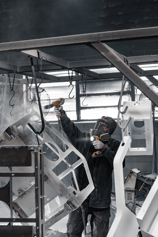Person powder coating a large metal structure in a workshop