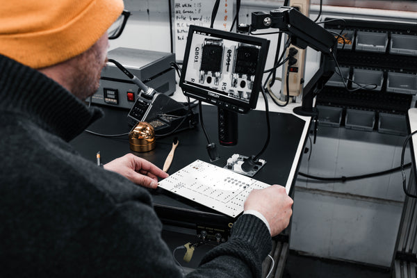 Person inspecting a circuit board and working with electronic equipment in a workshop setting