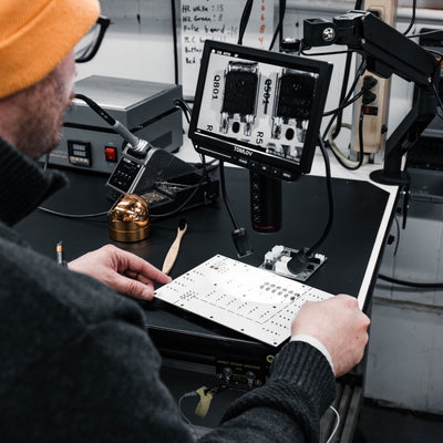 Person working on electronic components with a magnifying glass in a workshop setting