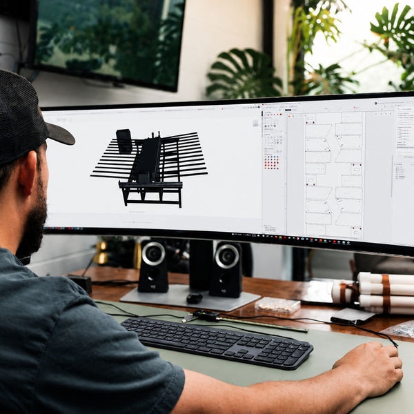 Engineer working at a desk with dual monitors, one displaying a 3D model of a machine.