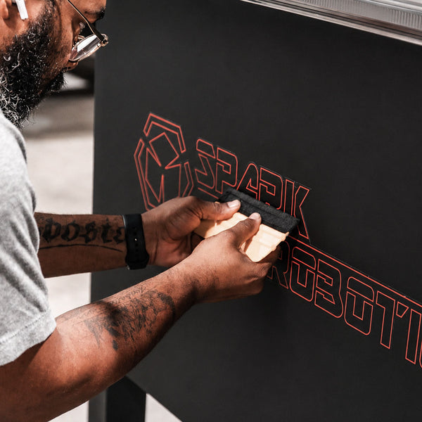 Person applying a logo to a black surface with a tool, featuring the brand 'Spark'.