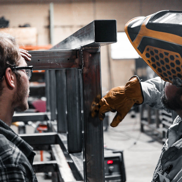 Two men working on a metal structure with one using a tool.