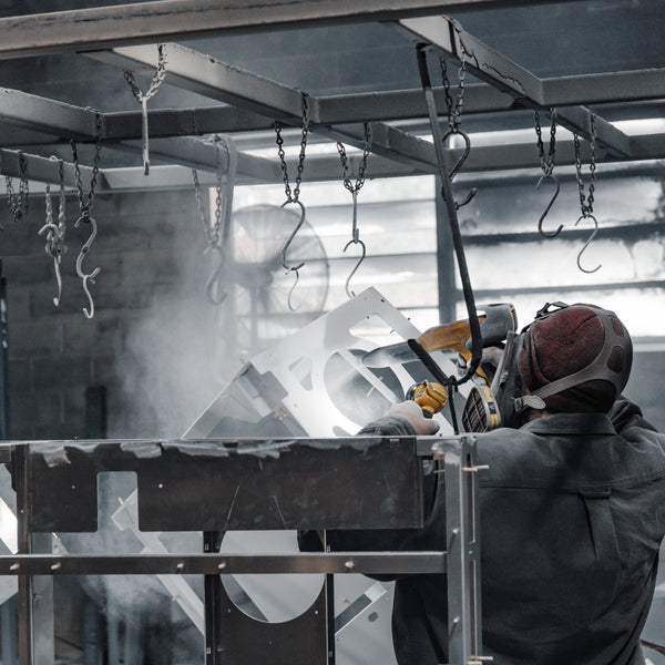 Person powder coating metal parts white in a warehouse setting