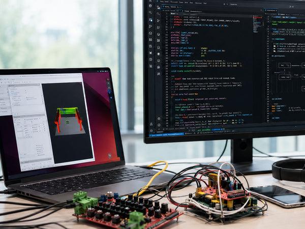 Laptop and monitor displaying code and 3D model on a desk