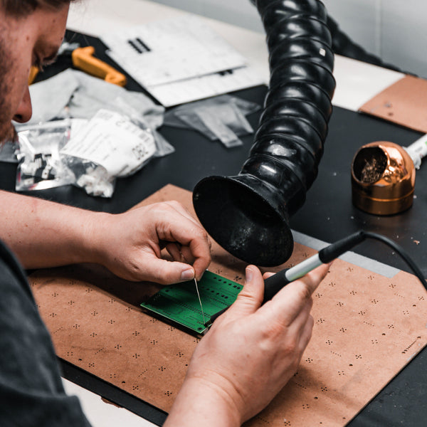 Person soldering on a small electronic component with tools on a workbench.